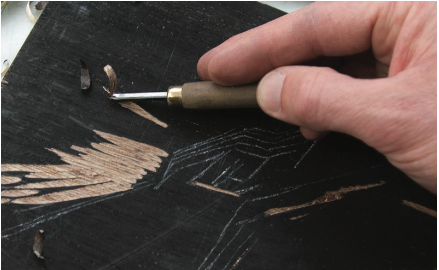 An image being carved into a piece of plywood using a woodcutting tool.